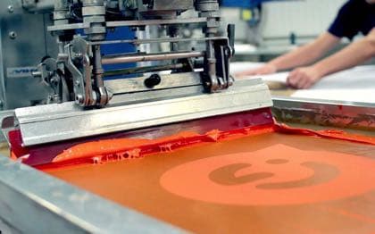 Screen printing press applying ink to fabric